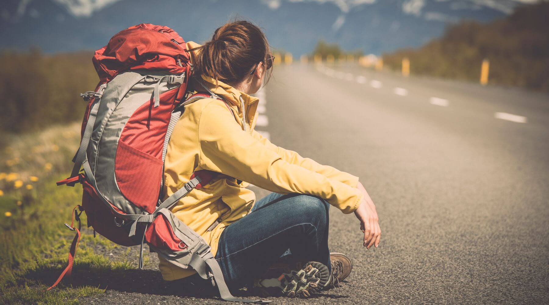 Woman sitting side of the road resting with a large hiking backpack
